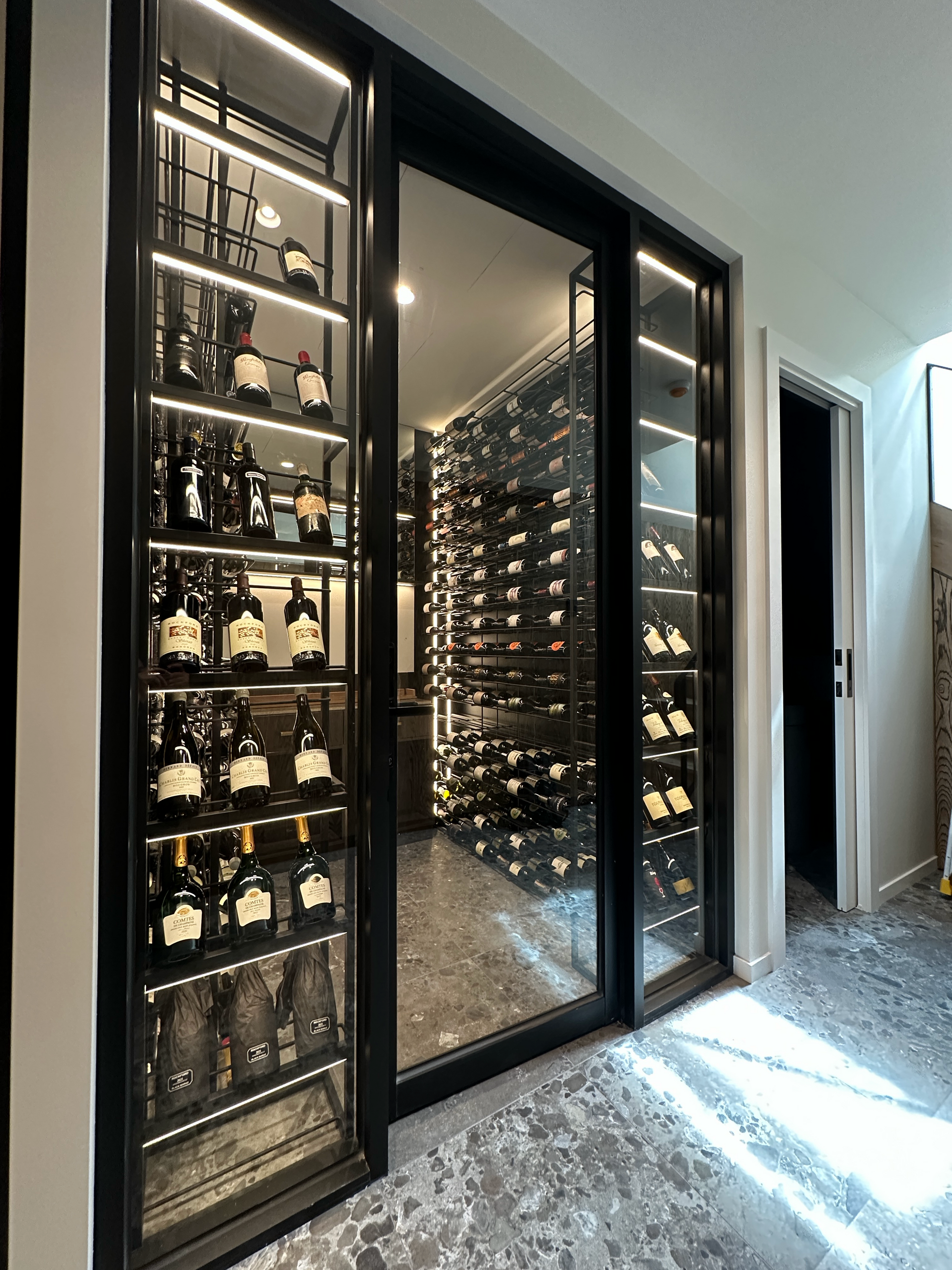 Wine cellar with glass door displaying rows of wine bottles.