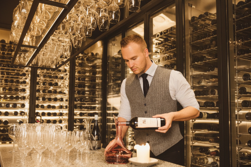 Man in a wine cellar pouring wine into a decanter